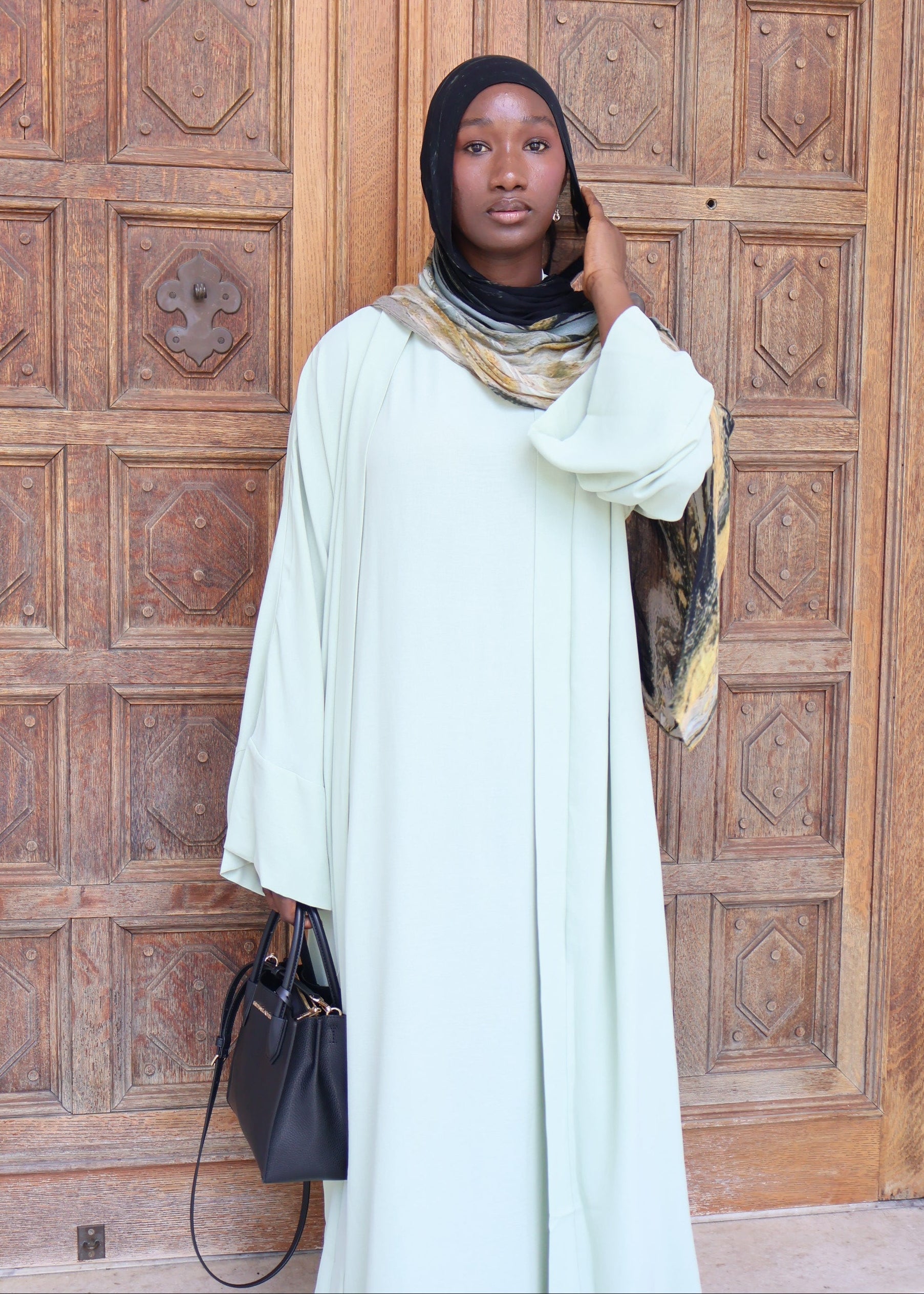 Woman in a light green dress standing in front of a wooden door